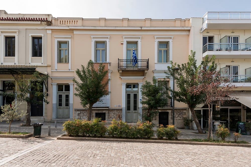 Charming Greek street with Museum Herakleidon historic buildings, cobblestone pavement, and Greek flag.