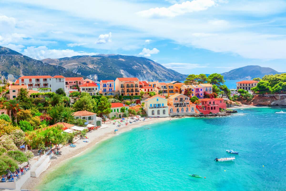 Beautiful Assos village in Kefalonia with colorful houses, sandy beach, turquoise waters, and mountain backdrop.