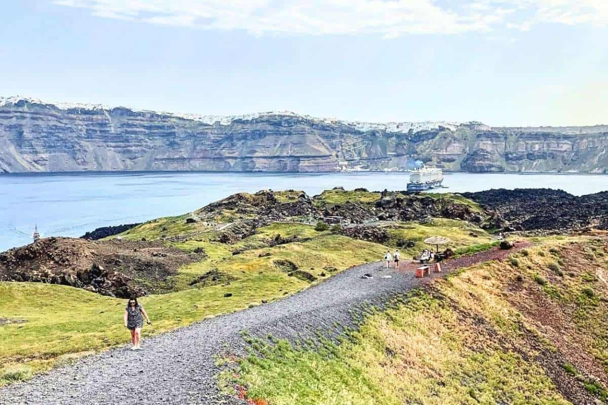 Scenic coastal hiking trail with cliffs, grassy hills, blue water, and a boat in Greece.