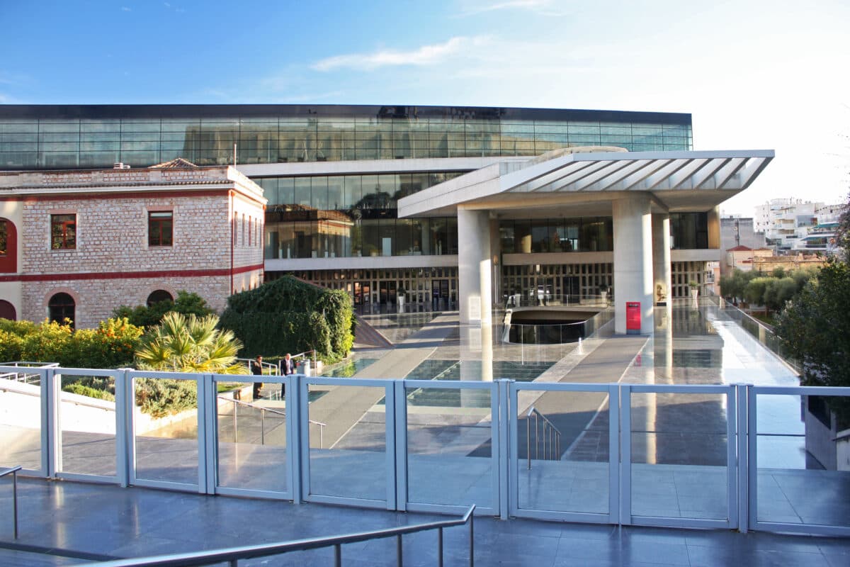 Modern Acropolis Museum in Athens with glass facade, classical architecture, greenery, and city views.
