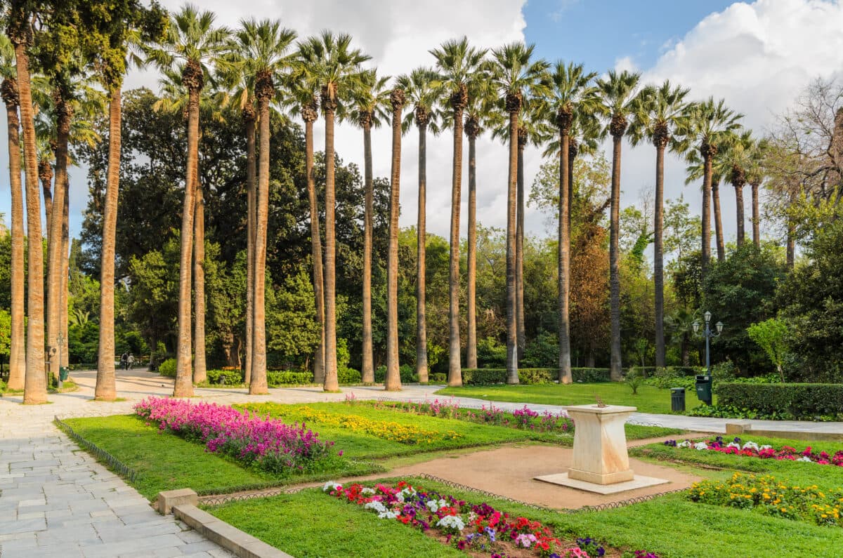 Beautiful Athens National Garden with palm trees, colorful flowers, and a stone sundial in Greece.