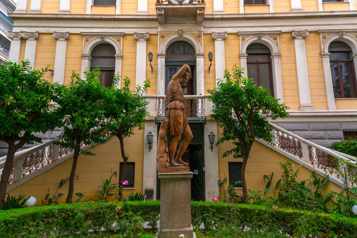 Entrance of Athens Numismatic Museum with classical architecture, sculptures, and lush garden.