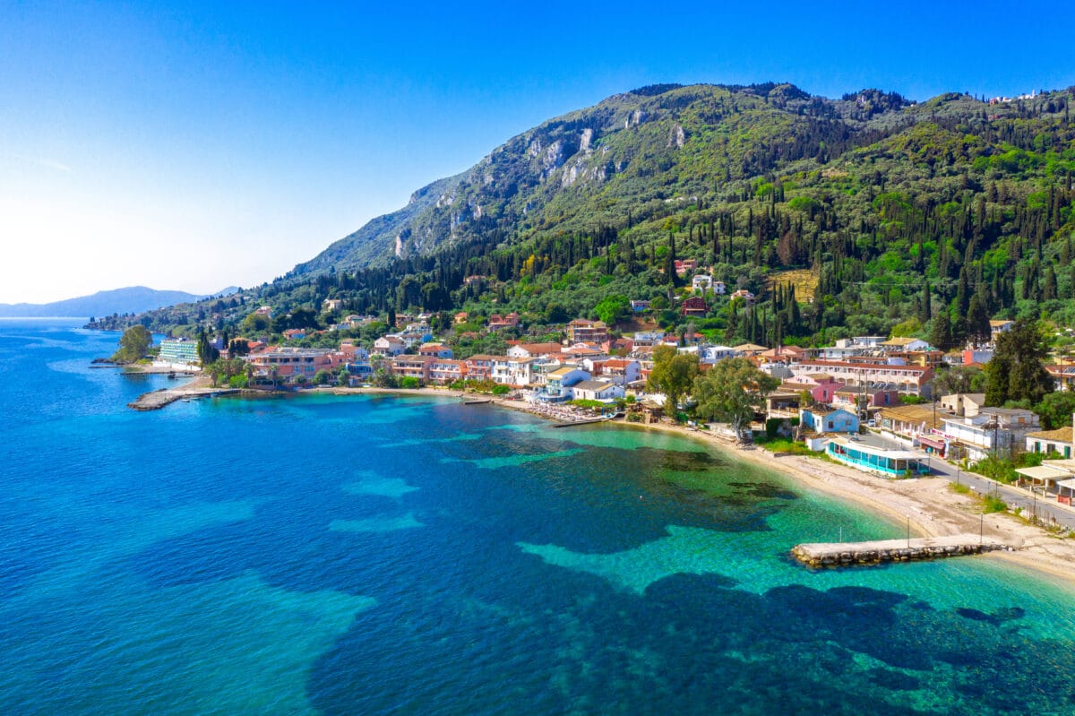 Benitses village in Corfu, Greece, with beautiful beaches, crystal-clear sea, Mediterranean mountains, and traditional architecture.