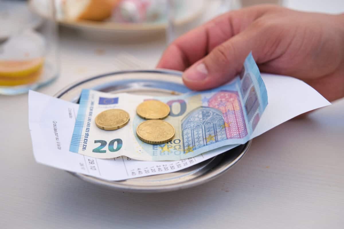 Customer returning euro cash tray with coins, banknote, and receipt at cafe or bar table.