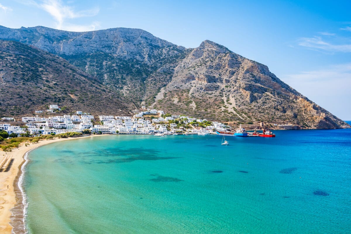 Scenic Greek island village at Kamares port, Sifnos with turquoise sea, sandy beach, and mountain backdrop.