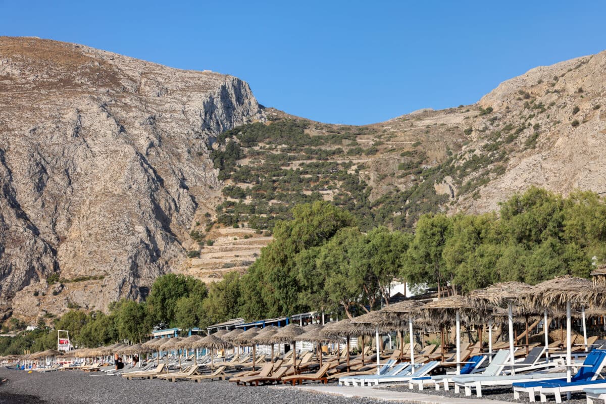 Sun loungers on Kamaris black volcanic beach in Santorini, Cyclades, Greece.