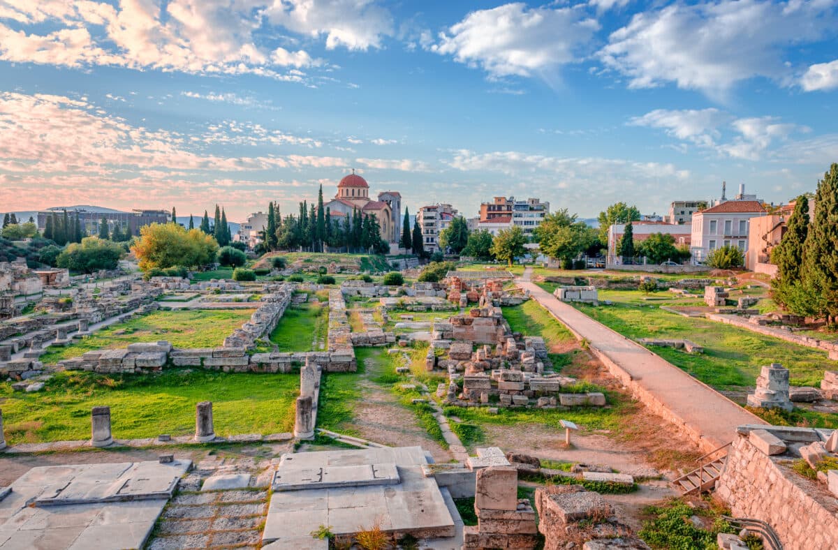 Ancient Kerameikos cemetery in Athens with the Holy Trinity Church, ruins, and modern city backdrop.