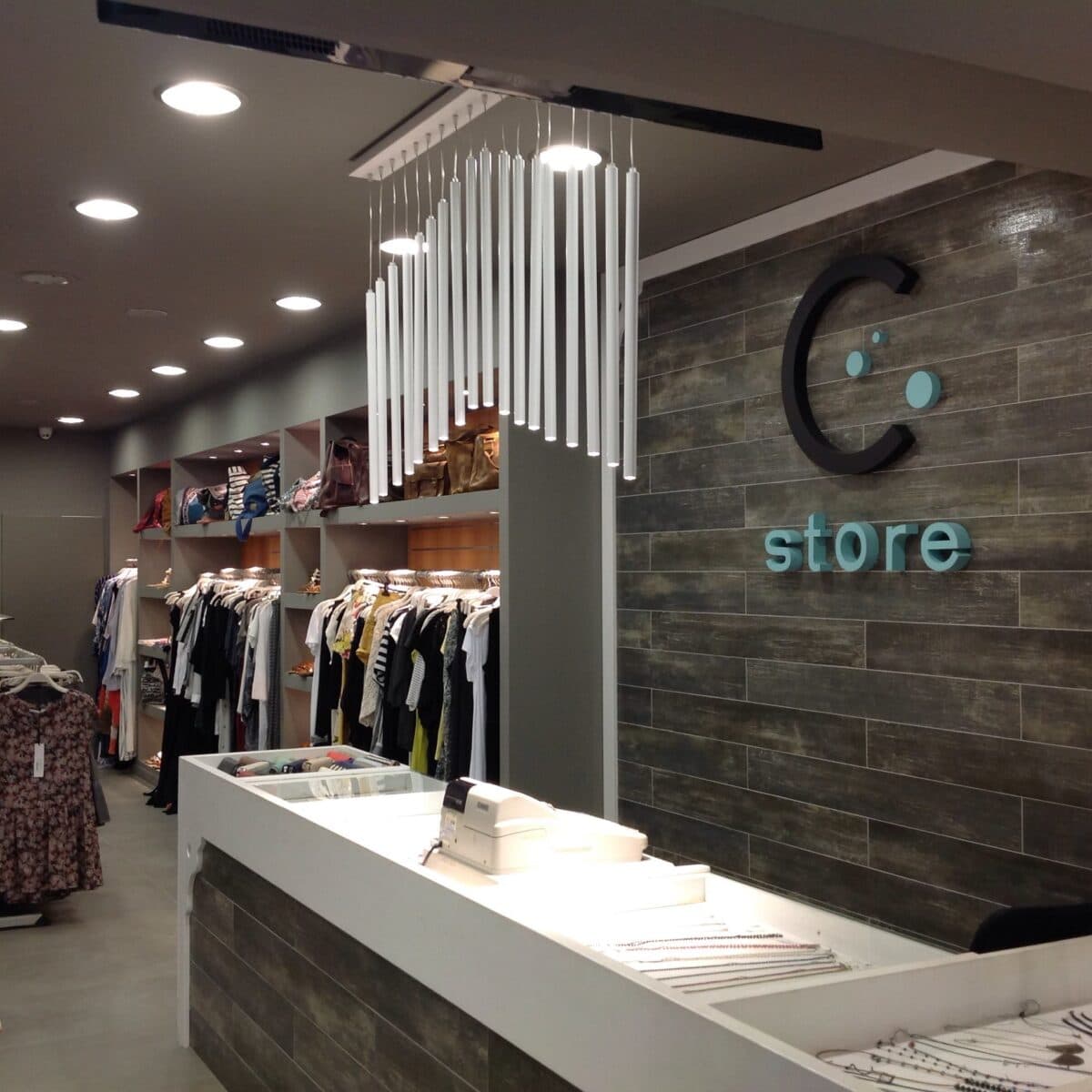 C Store Santorini boutique clothing store interior with checkout, jewelry displays, clothing racks, and stylish lighting.