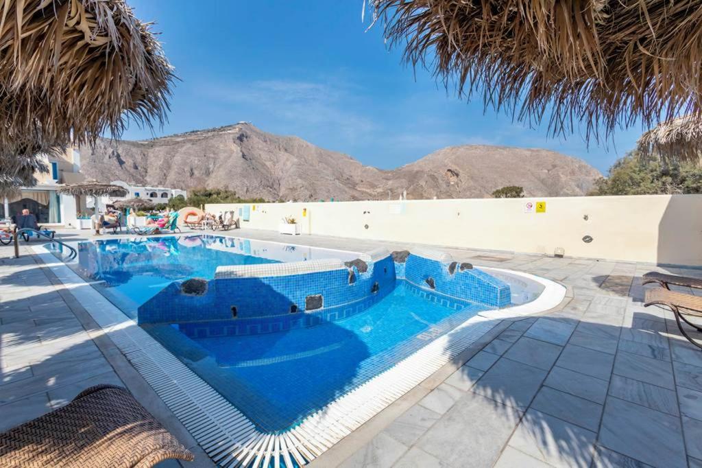 Perissa Bay Hotel swimming pool with loungers, sunshade umbrellas, and rocky desert mountain backdrop.