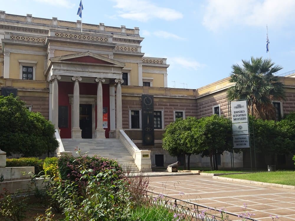National History Museum (Old Parliament) with classical architecture, marble stairs, lush greenery, and blue sky.