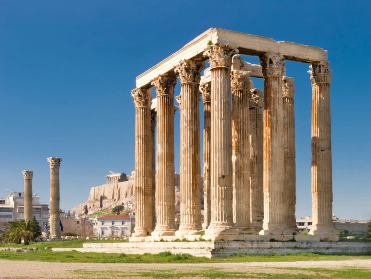 Ancient Olympieion temple ruins with Corinthian columns and the Acropolis of Athens in the background.
