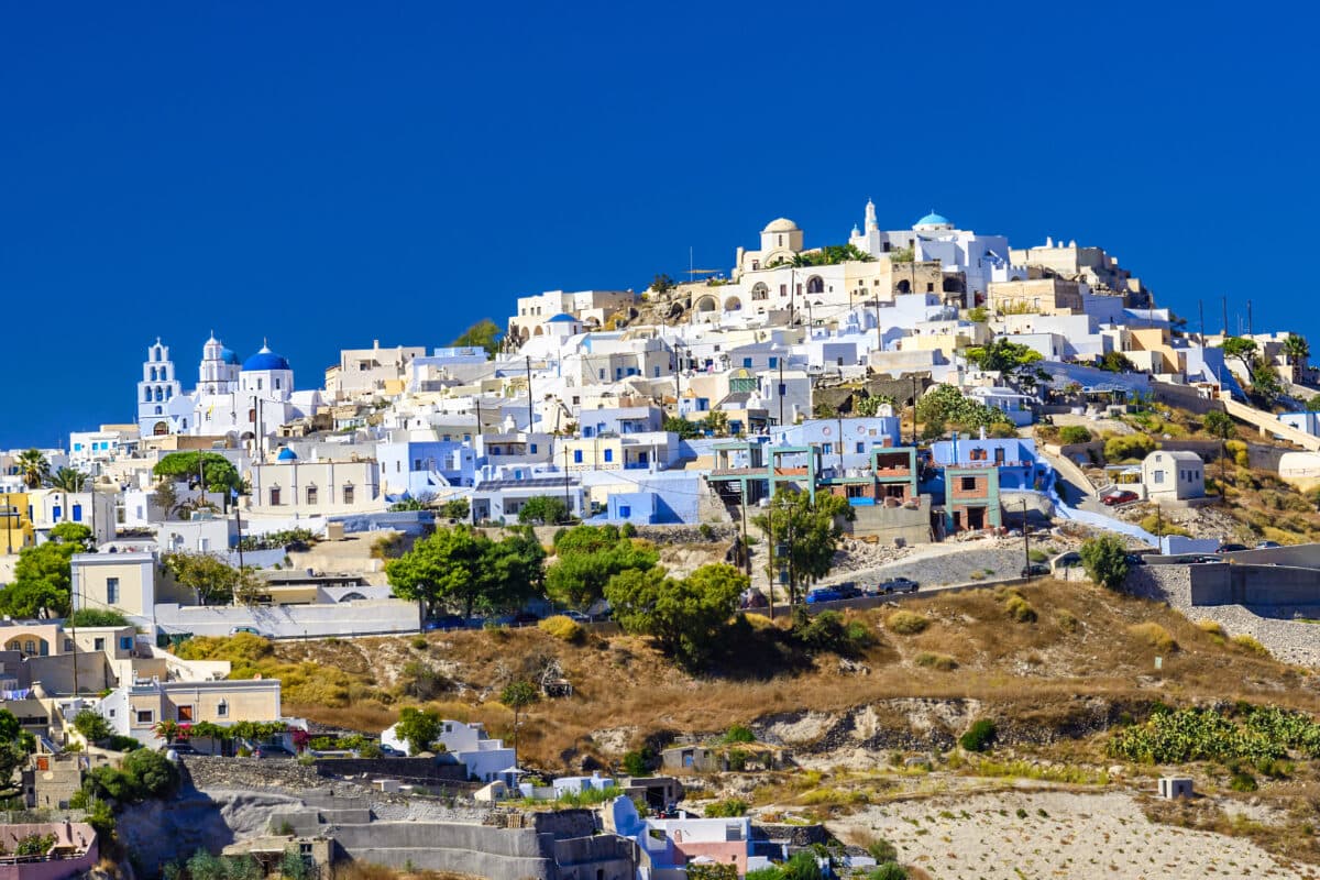 Charming Pyrgos Kallistis village in Santorini with white buildings, blue domes, and panoramic Aegean views.