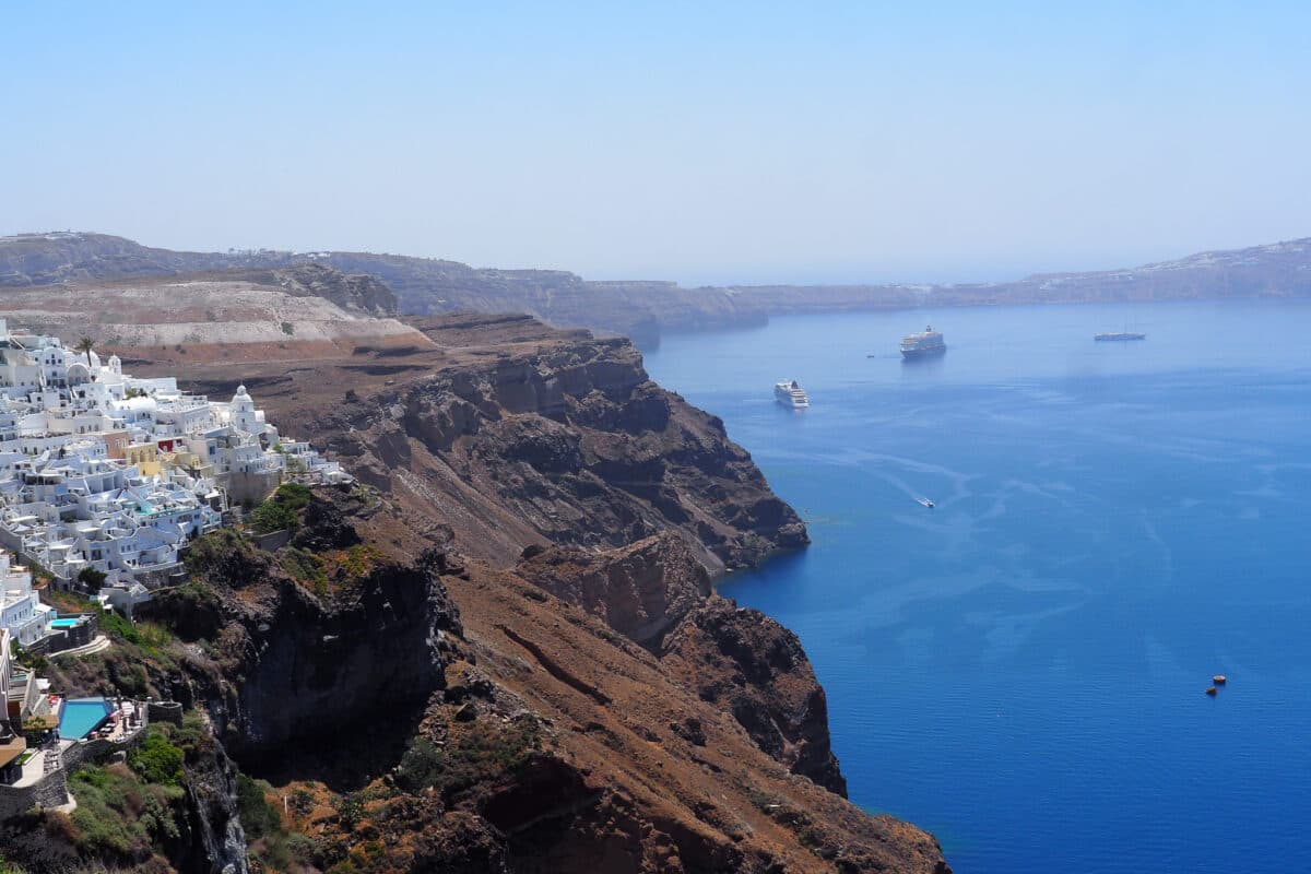 Scenic view of Santorinis Fira cliffside town and blue caldera bay with boats and volcanic cliffs.