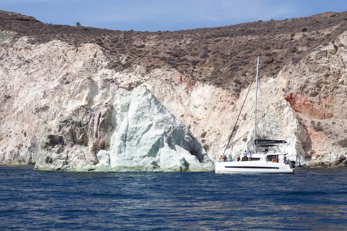 White Beach in Santorini featuring white cliffs, blue waters, a sailboat, and rugged coastal scenery.